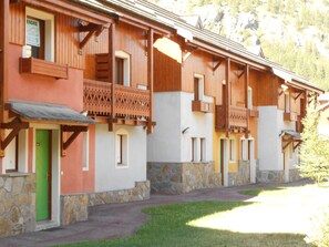 A row of wooden buildings with balconies, stone foundations, and a green door. - Semi-detached chalet south, shuttle to slope - 7 guests (La Salle-les-Alpes)