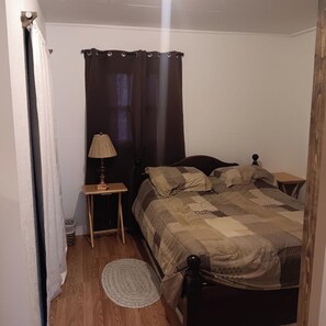 A bedroom with a bed, a nightstand, a lamp, a rug, and a curtain.