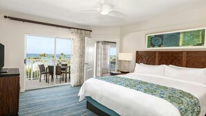 A hotel room with a large bed, a television, a desk with chairs, and a balcony with a view of the ocean. - Spacious Family Friendly Resort in Aruba-Oceanfront, Amenities, Water Sports (Noord)