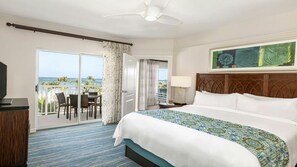 A hotel room with a large bed, a television, a desk with chairs, and a balcony with a view of the ocean. - Spacious Family Friendly Resort in Aruba-Oceanfront, Amenities, Water Sports (Noord)