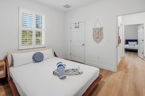 Ein Schlafzimmer mit einem Bett, einem Fenster mit Jalousien, einer Tür und einem Wandbehang aus Makramee.