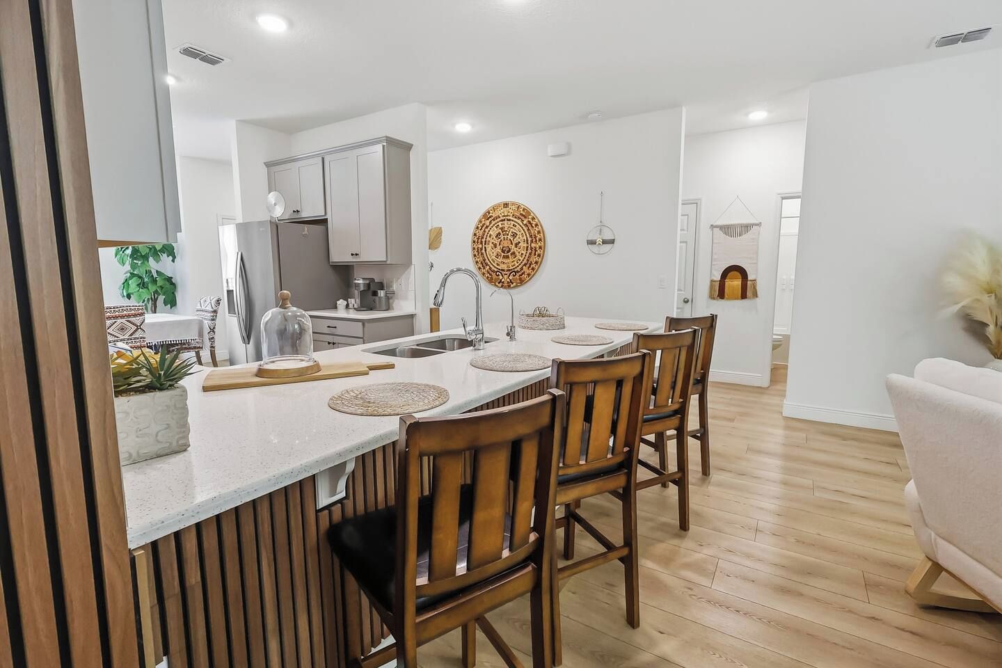 A modern kitchen with a central island, wooden chairs, and a dining table.