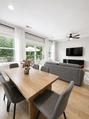 Una sala de estar moderna con una mesa de comedor, un sofá gris y un televisor de pantalla plana montado en la pared.