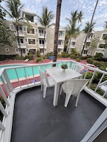 A poolside area with a table and chairs, surrounded by a railing, and overlooking a swimming pool.