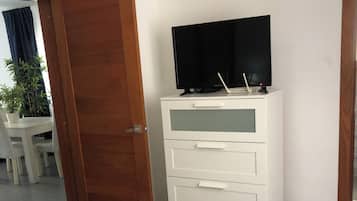 Ein Hotelzimmer mit einem Bett, einer weißen Kommode mit Schubladen, einem Fernseher darauf und einer Tür zu einem anderen Raum.