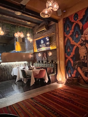 Et restaurantinteriør med hængende lys, en murstensvæg, et muralmaleri og et skilt med teksten 'MAZAL'.