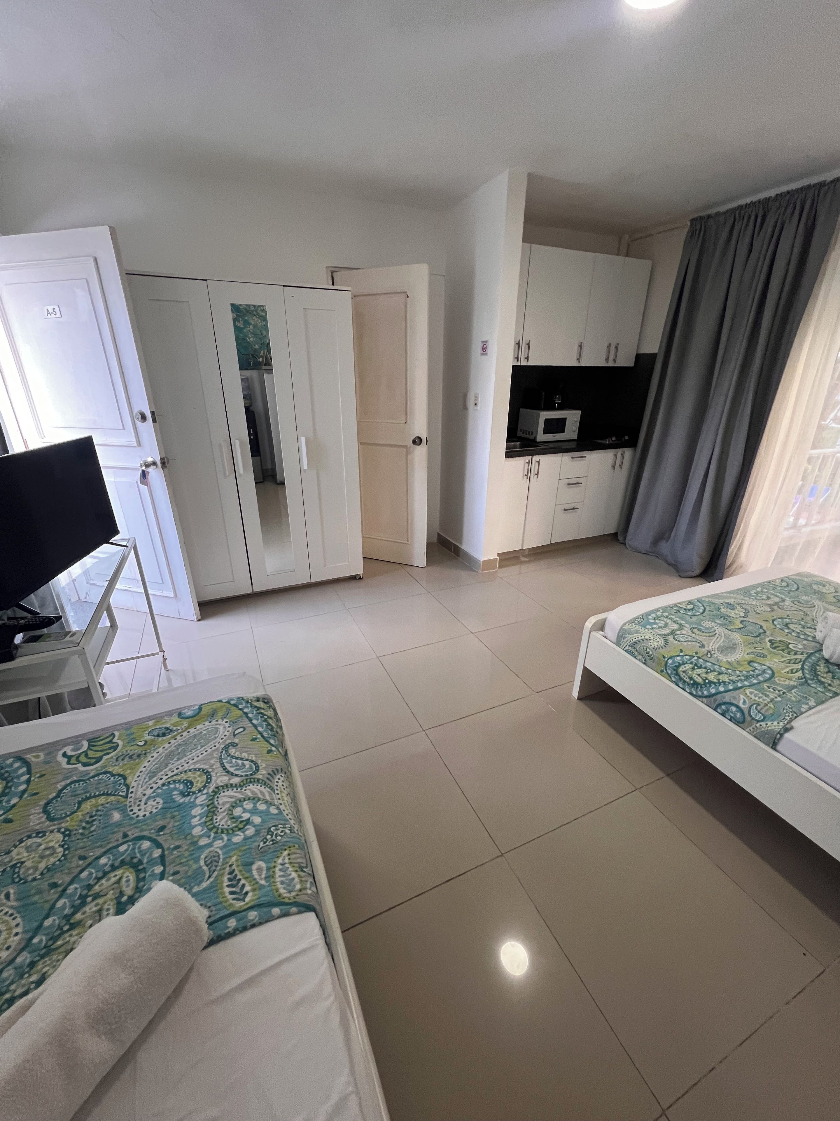 Quarto de hotel com duas camas, uma cozinha compacta e banheiro.