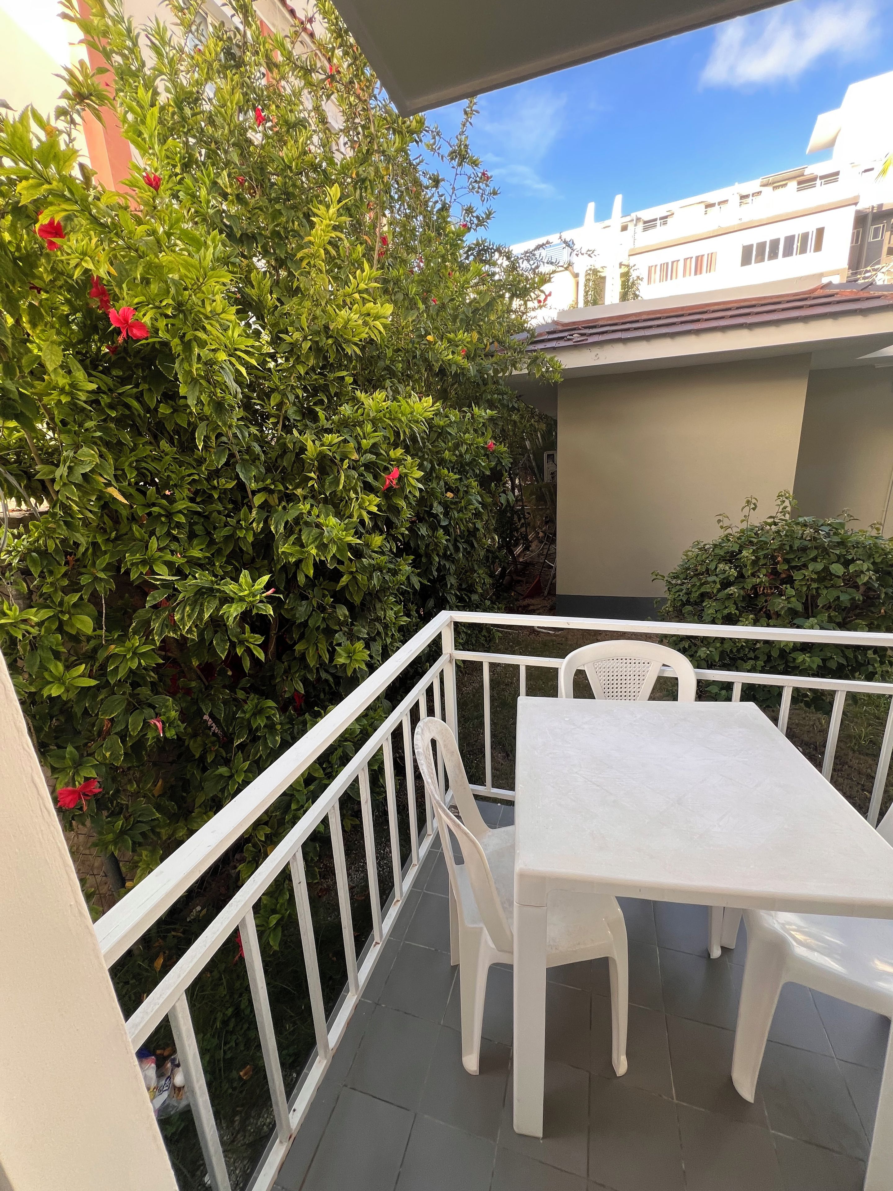 Un balcon avec une table et des chaises blanches, entouré de verdure et doté d’une balustrade blanche.