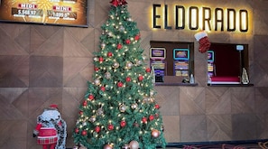 Un árbol de Navidad decorado frente a una pared con la palabra 'ELDORADO' y una máquina tragamonedas.