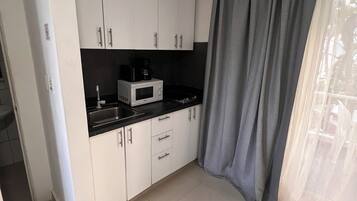 Una cocina con armarios blancos, encimera negra, microondas y cafetera.