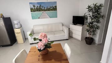 Un espacio habitable compacto con una mesa de comedor, un sofá blanco y un televisor sobre un mueble.