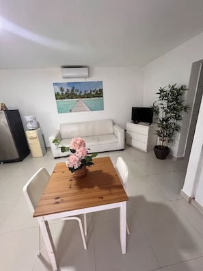 Un espacio habitable compacto con una mesa de comedor, un sofá blanco y un televisor sobre un mueble.