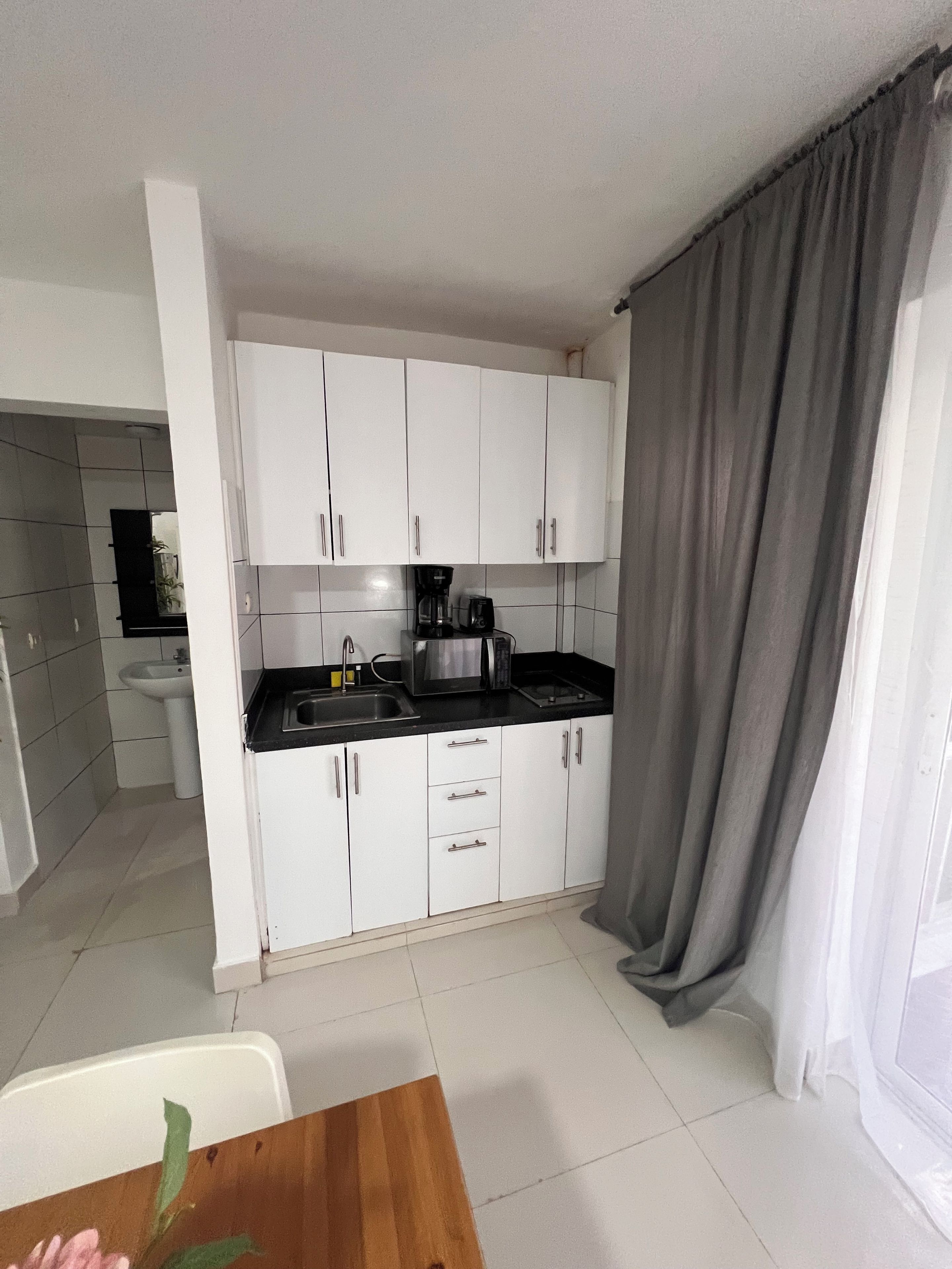 Cocina compacta con armarios blancos, encimera negra y cafetera.