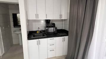 Cocina compacta con armarios blancos, encimera negra y cafetera.