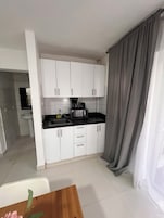 A compact kitchen with white cabinets, a black countertop, and a coffee maker.