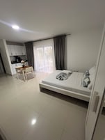 A bedroom with a bed, a desk, and a kitchenette.