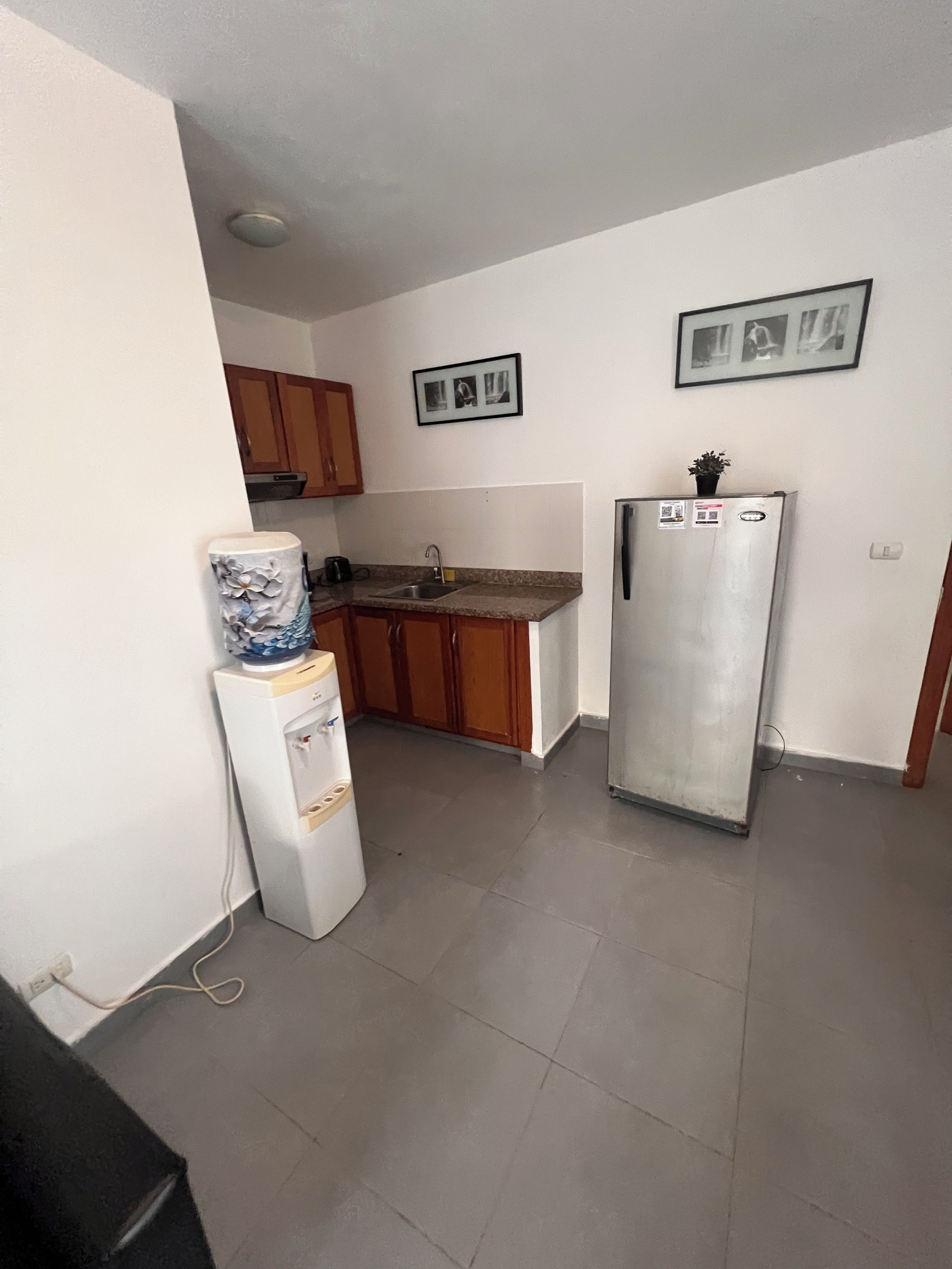 Una cocina compacta con armarios de madera, un refrigerador y un dispensador de agua.
