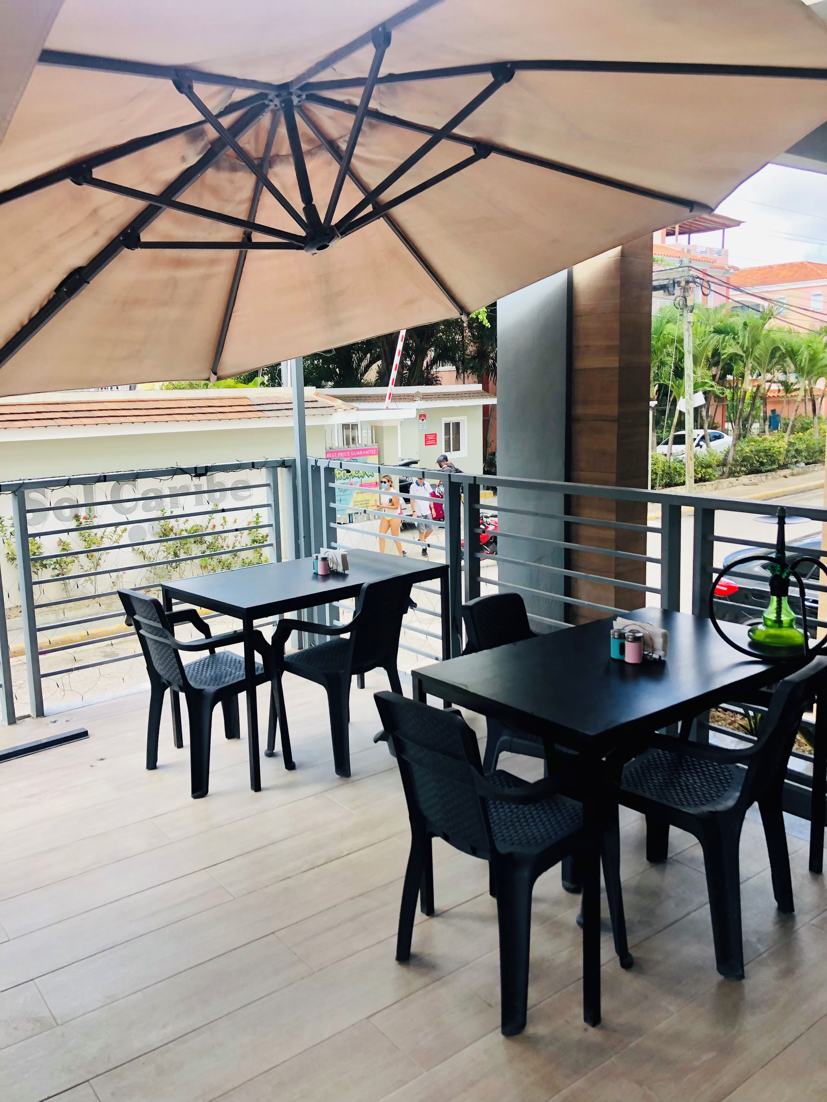 An outdoor seating area with tables and chairs, a large umbrella, and a view of the street.