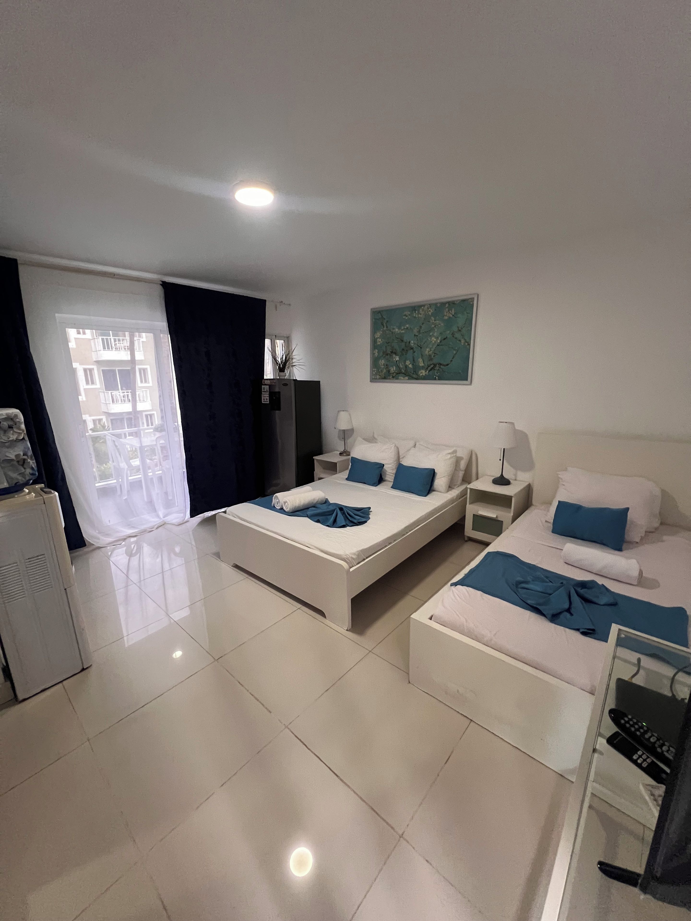 Habitación de hotel con cama, escritorio, silla, lámpara, un cuadro y vistas al exterior.