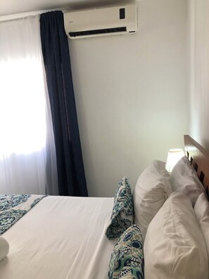 A hotel room with a bed, a window with curtains, an air conditioning unit, and a bedside lamp. - Sol Caribe Tropical Beach Suites (Punta Cana)