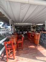 An outdoor seating area with wooden tables and chairs, a bar counter, and a sign for Los Corales Cigar Gallery.