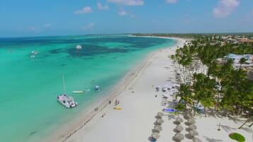 Una playa con aguas turquesas cristalinas, una orilla arenosa y una hilera de palmeras.