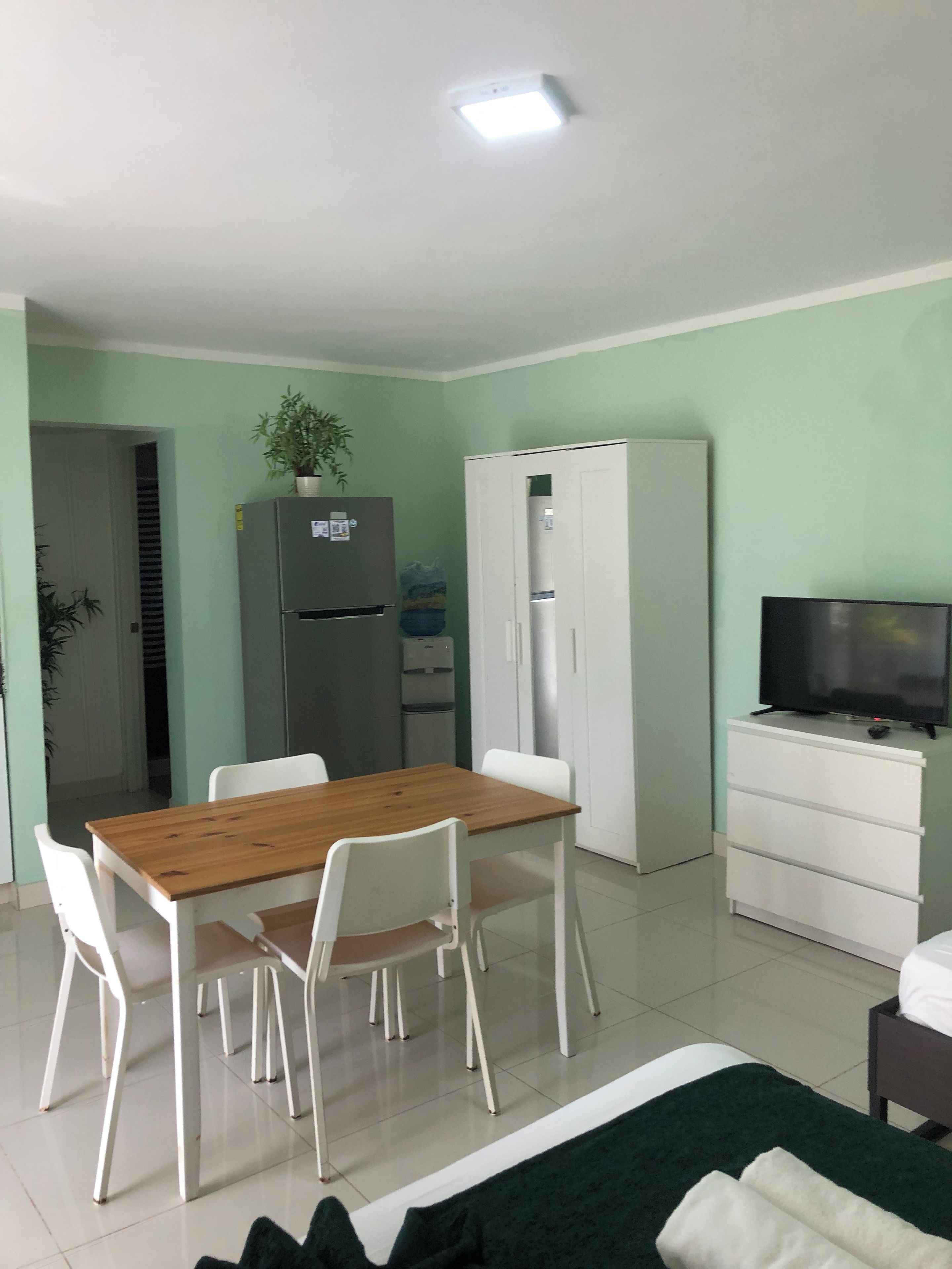 Un espacio habitable funcional con mesa, sillas, refrigerador, armario, televisor y cama.