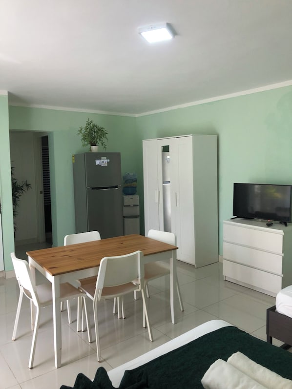 Un espacio habitable funcional con mesa, sillas, refrigerador, armario, televisor y cama.
