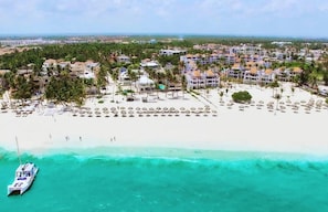 Un resort costero con villas frente a la playa, una playa de arena y un barco amarrado cerca de la orilla.