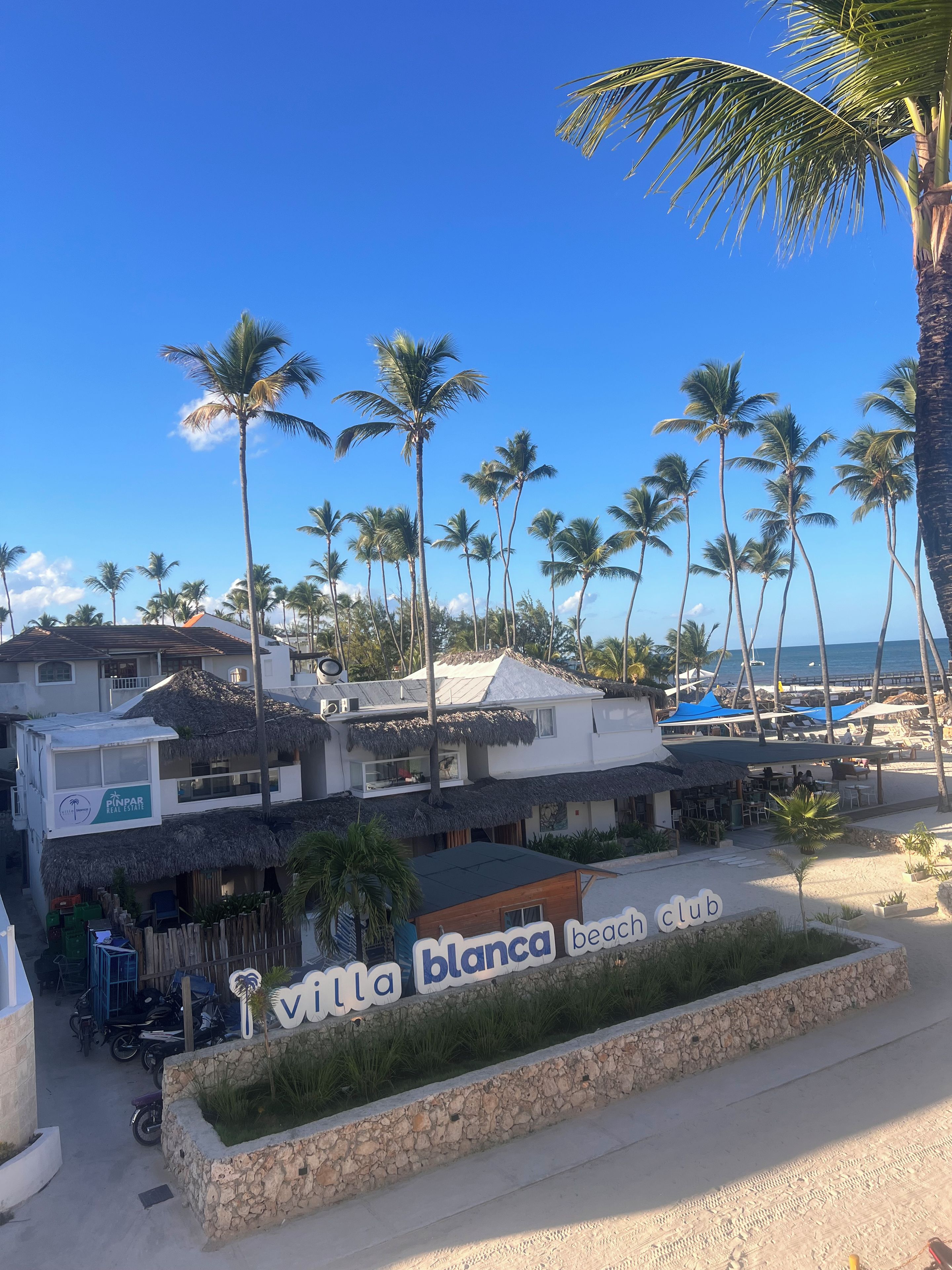 Un club de plage avec une enseigne, des palmiers et une plage en arrière-plan.