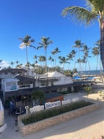 A beach club with a signboard, palm trees, and a beach in the background.
