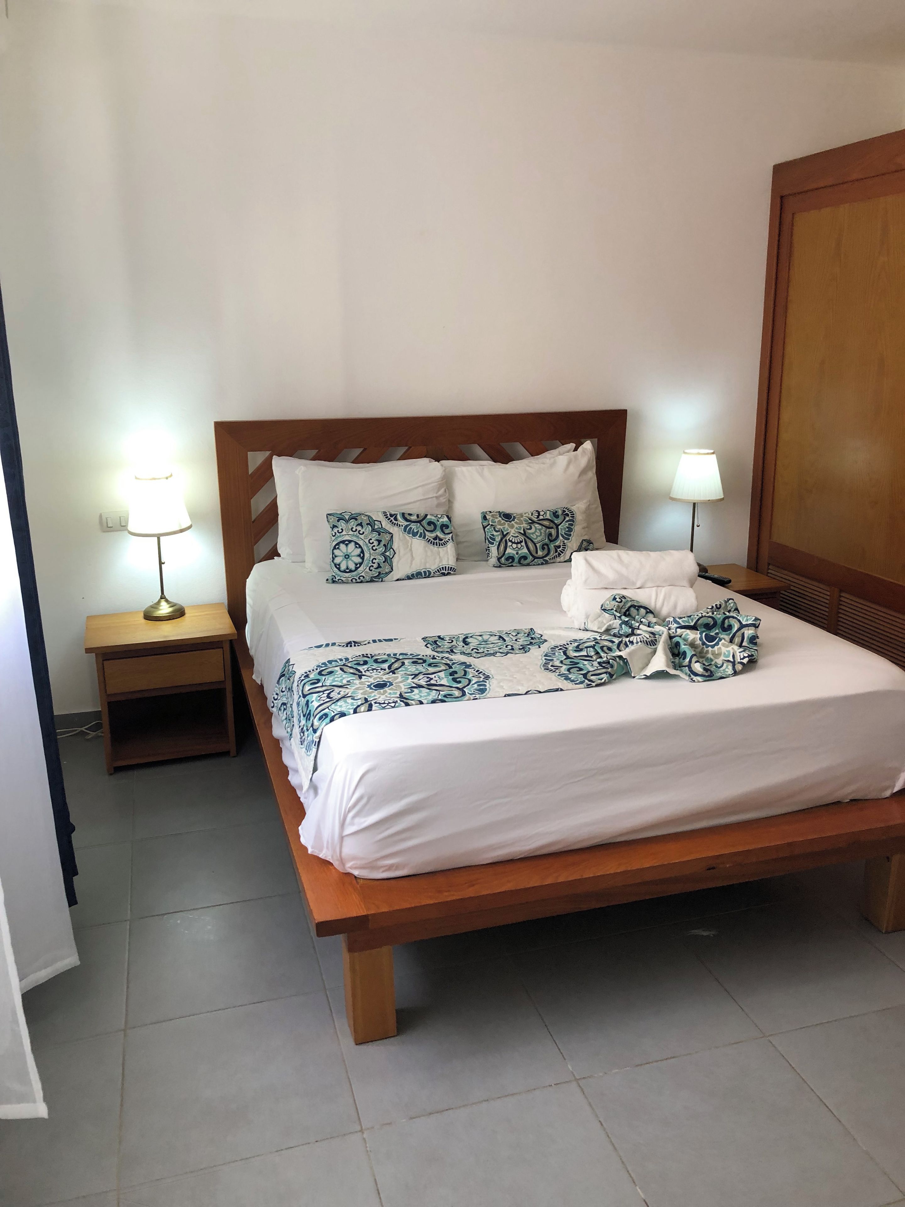 Una cama bien hecha con ropa de cama estampada, un cabecero de madera y lámparas de noche.