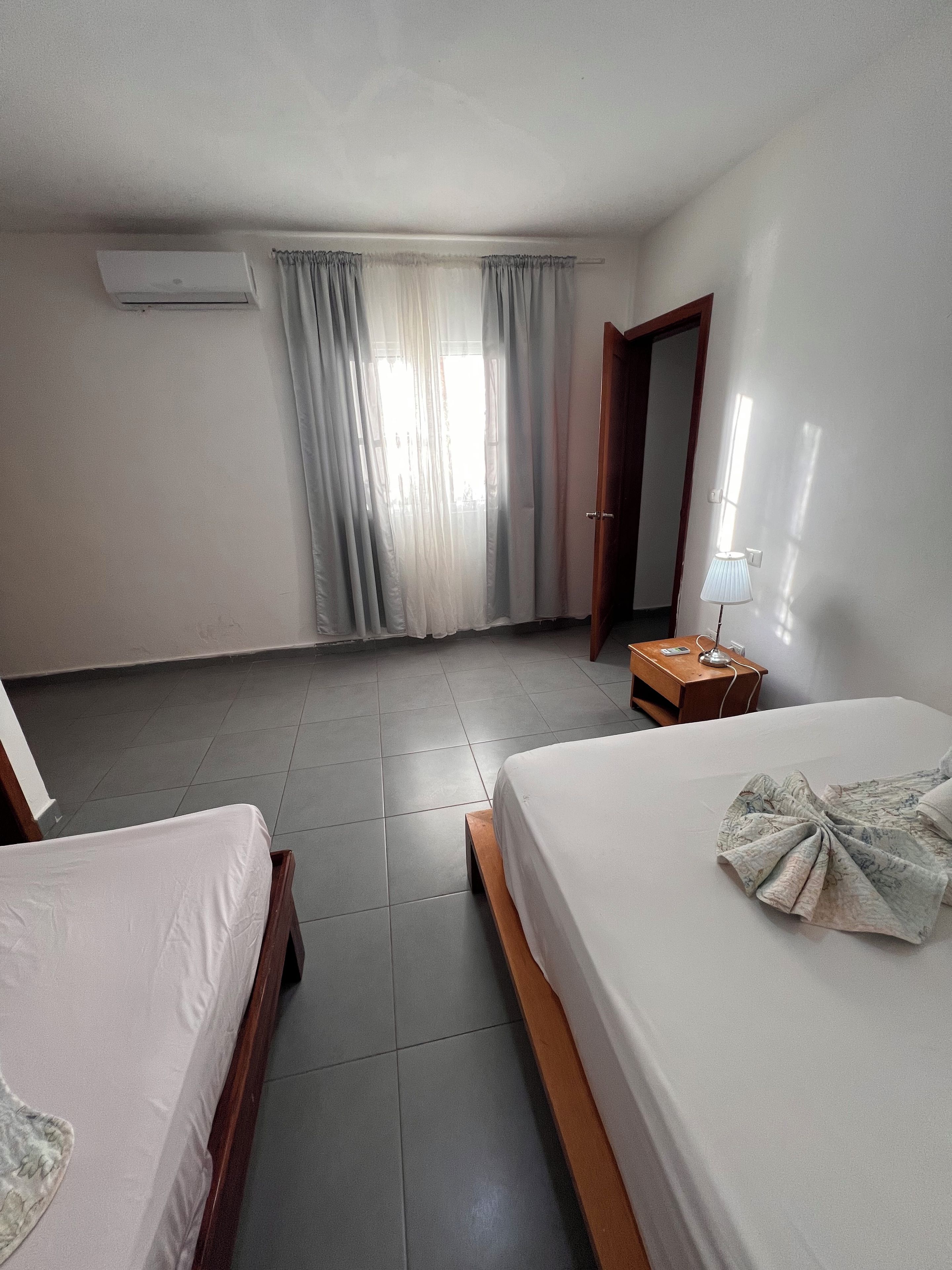A hotel room with two beds, a desk with a lamp, and a window with curtains.