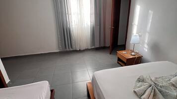 A hotel room with two beds, a desk with a lamp, and a window with curtains.