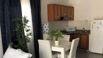Habitación de hotel con cama, mesa de comedor, sillas, planta en maceta, microondas y refrigerador.