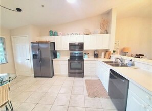 A modern kitchen with white cabinets, stainless steel appliances, and a glass dining table. - Spacious 2-bedroom Condo with Golf course views in beautiful Naples (Naples)