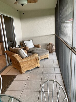 Un balcon avec des meubles en osier, une porte vitrée et une chaise en métal.