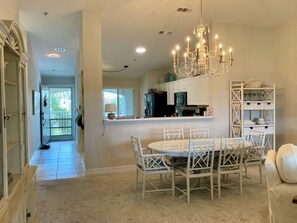 A dining area with a chandelier, white chairs, and a white table. - Spacious 2-bedroom Condo with Golf course views in beautiful Naples (Naples)