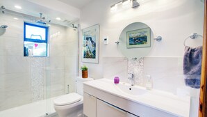 Un baño moderno con cabina de ducha de vidrio, inodoro, tocador con lavabo y espejo.