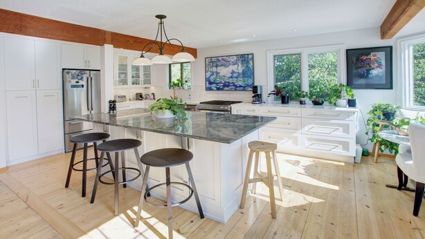 Una cocina moderna con una isla grande, taburetes de bar y mucha luz natural.