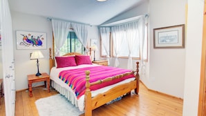 Un dormitorio con cama de madera, cortinas blancas, alfombra blanca y obras de arte en las paredes.