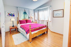 Un dormitorio con cama de madera, cortinas blancas, alfombra blanca y obras de arte en las paredes.