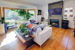 Amplia sala de estar con chimenea, un sofá y un ventanal con vistas a un jardín.