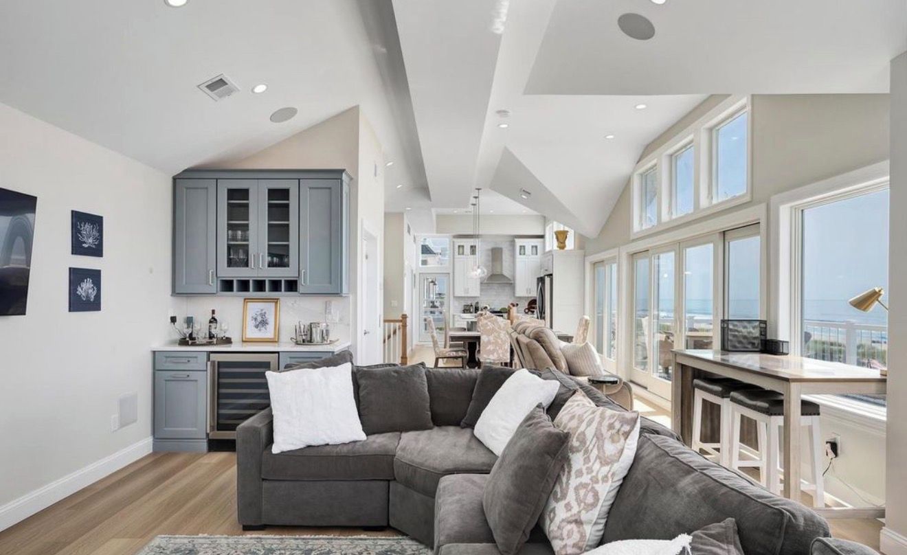 A modern kitchen with grey cabinets, a dining area with a high table, and a large window overlooking a balcony.