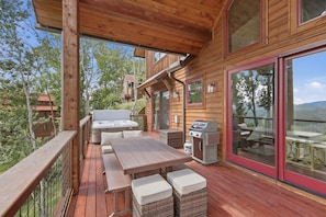Grill up dinner, then carry it straight to the long table with its bench and woven stools, all sheltered beneath a wood-plank roof. The hot tub anchors the far end, and red-framed glass doors lead back inside the moment someone wants seconds. - Bear Cub Lodge Gated 3BR Eagles Nest Lodge with Hot Tub, Sleeps 10 (Banner Elk)