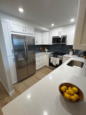 A modern kitchen with white cabinetry, stainless steel appliances, and a granite countertop. - Sunsets at 19 Beachfront Penthouse Condo (Marco Island)