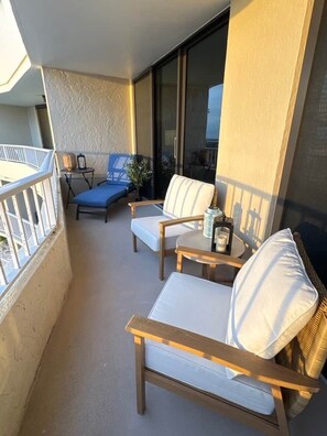 A balcony with two cushioned chairs, a small table, and a potted plant. - Sunsets at 19 Beachfront Penthouse Condo (Marco Island)