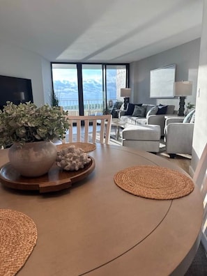 Un salon moderne avec une table en bois aux lignes courbes, une plante en pot et une vue sur les montagnes, visible à travers de grandes fenêtres.