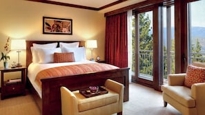 Quarto de hotel com uma cama grande, duas mesas de cabeceira, uma cadeira, uma pequena mesa com bandeja e uma varanda com vista.