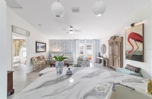 A spacious living room with a marble coffee table, a ceiling fan, and a large painting of a flamingo. - Elegant & Cozy 3-Bedroom Home in Ocala – Perfect for a Relaxing Stay (Ocala)
